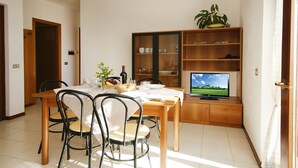 Uma área de refeições com uma mesa de madeira, quatro cadeiras, uma televisão sobre um suporte de madeira e uma estante com portas de vidro.