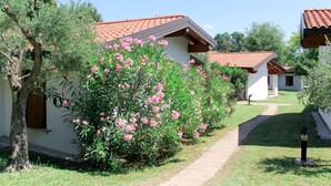 A row of white buildings with red-tiled roofs, surrounded by greenery and a clear sky.