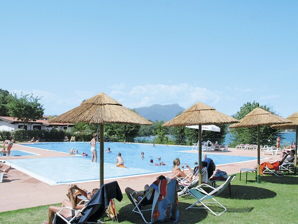 A pool area with multiple umbrellas, lounge chairs, and people swimming and relaxing.