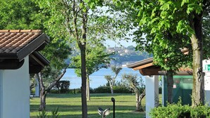 A serene garden with a pathway leading to a gazebo, surrounded by lush greenery and a view of a lake with buildings in the distance.