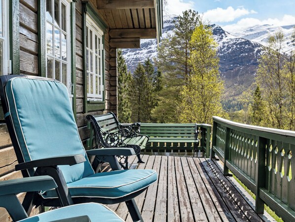 Una terraza de madera con dos sillas y un banco, con vistas a un paisaje montañoso.