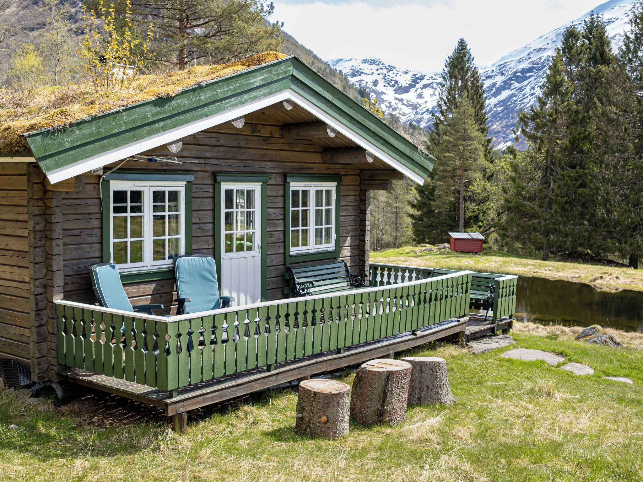 Een blokhut met een groene veranda, een houten terras en uitzicht op een meer en bergen.