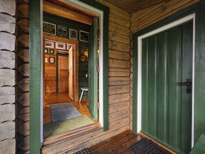 Una cabaña de madera con puerta verde, un pasillo interior visible y un pequeño porche.