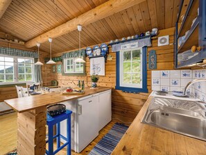 Interior de una cabaña de madera con cocina, comedor y ventana con vistas a la vegetación.