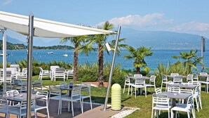 Een terras met witte stoelen en tafels, met uitzicht op een waterpartij met boten en een verre kustlijn.