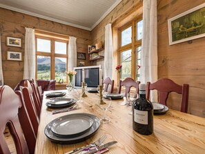 A dining room with a wooden table set for a meal, a television, and framed artwork on the walls.