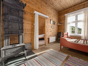 A wooden room with a bed, a chair, a radiator, and a window with a view.
