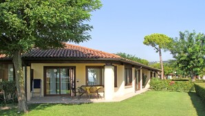 A two-story house with a tiled roof, a covered patio with chairs, and a well-maintained lawn.
