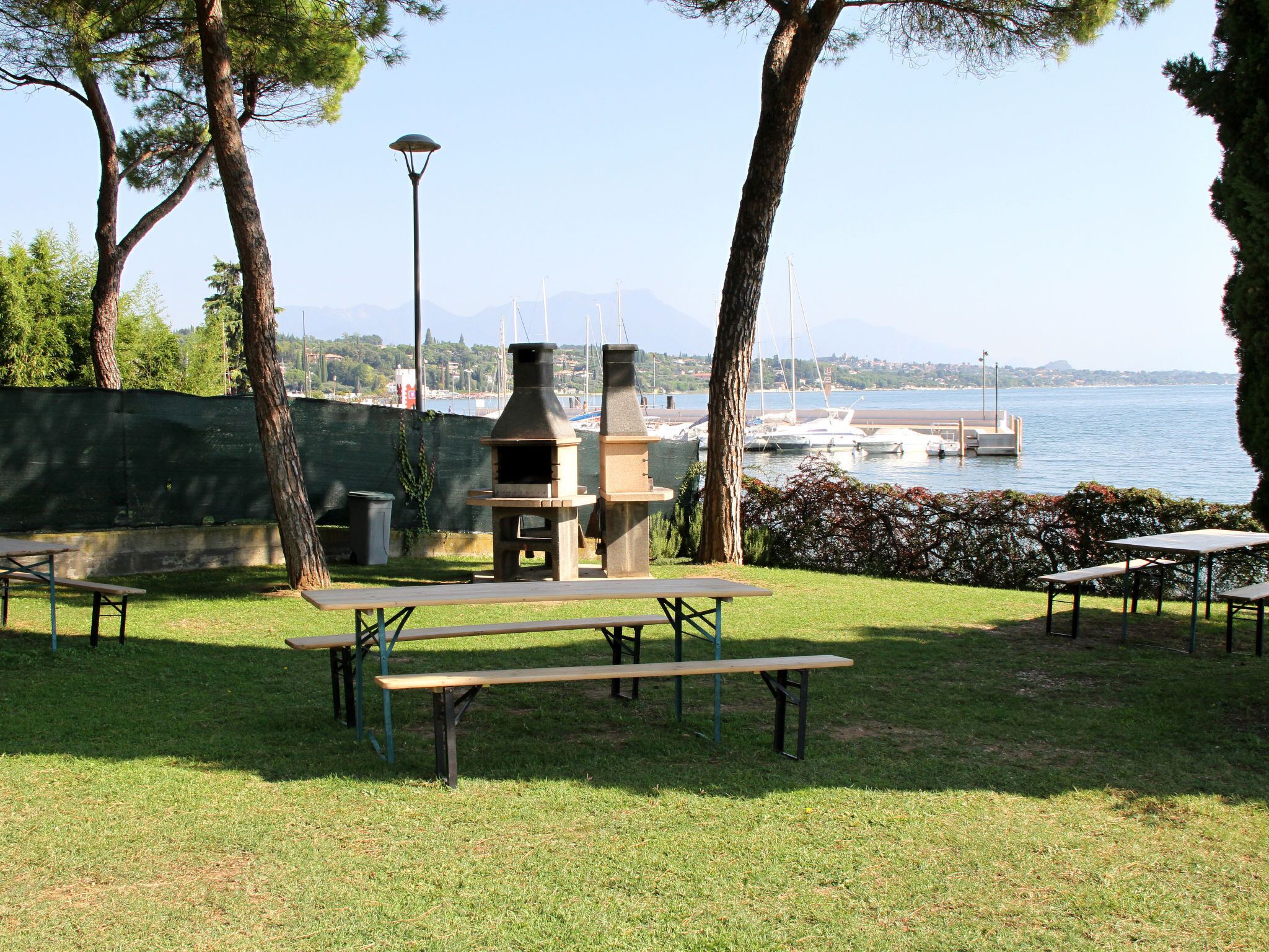 Une terrasse extérieure avec des tables de pique-nique, un four à bois et une vue sur une marina et des montagnes.