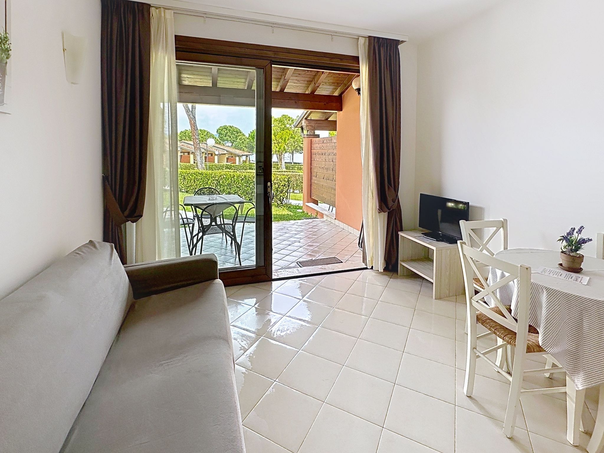 Ein Hotelzimmer mit einer Couch, einem Esstisch mit Stühlen, einem Fernseher und einer Schiebetür zu einem Außenbereich mit Tisch und Stühlen.