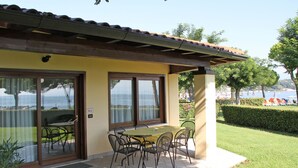 A patio with a table and chairs, a view of the sea, and a building with a yellow facade.