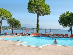 Et poolområde med liggestole og parasoller, fri udsigt til havet og et bjerglandskab i baggrunden.