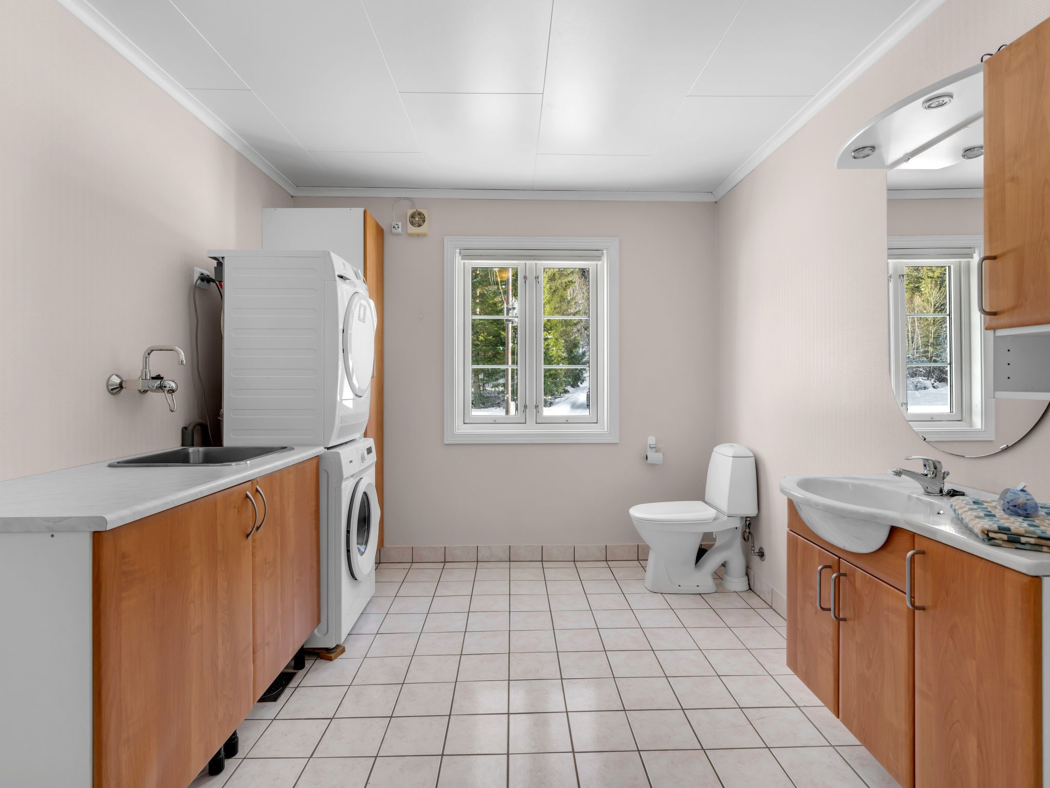 Un baño moderno con lavadora, inodoro, lavamanos y un ventanal con vista a árboles.