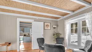 A cozy living room with wooden floors, two grey armchairs, a white door leading to a kitchen, and a large window with a view of the outdoors. - Vacation home Haven by Interhome (Birkeland)