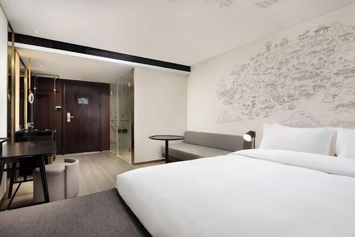 A modern hotel room with a bed, a desk, a sofa, and a wall with a detailed mural.