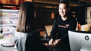 En person står ved en disk i en restaurant, med et udstillingsvindue med mad i baggrunden.