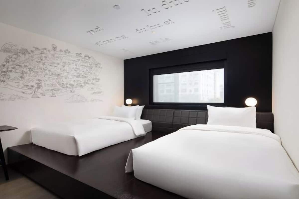 A modern hotel room with two beds, a dark headboard, a large window, and a wall mural.