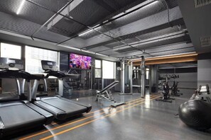 Ein Fitnessstudio mit Laufbändern, Kraftgeräten und einem Fernsehbildschirm.