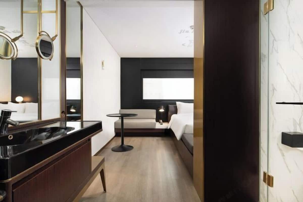 A modern hotel room with a large mirror, a black countertop, a small round table, a bed with white bedding, and a large window.