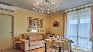 Ein Wohnzimmer mit einem beigefarbenen Sofa, einem Esstisch für vier Personen und einer Deckenleuchte.