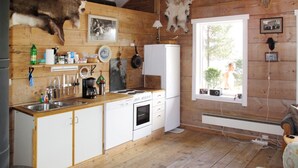 Une cuisine rustique aux murs en bois, ornée d’une tête de cerf fixée au mur, et dotée d’une fenêtre donnant sur un paysage verdoyant.