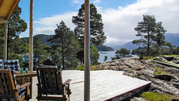 Une terrasse en bois avec deux chaises et une table, offrant une vue sur un lac et des montagnes.