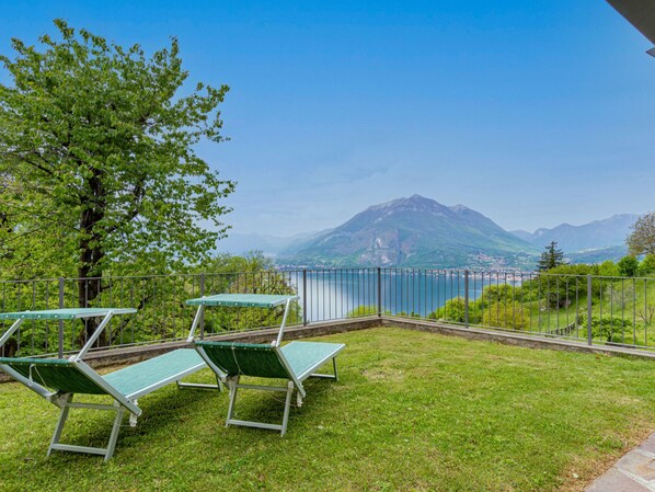 A grassy outdoor area with green lounge chairs and a scenic view of a lake and mountains.