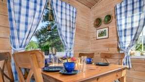 A wooden cabin interior with a dining table set for four, blue and white checkered curtains, and a view of greenery outside. - Synnøve by Interhome (Hellevik I Fjaler)
