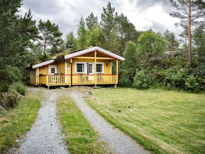 En gul hytte med veranda, omgivet af træer og en grussti.