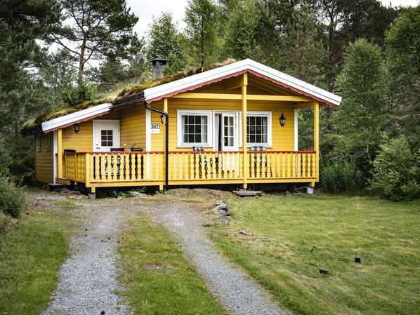 En gul hytte med rødt tag, veranda og skilt med nummer 547.