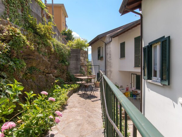 A narrow alleyway with a stone pathway, a wooden table with chairs, and a balcony with green shutters. - Vacation home Gaia by Interhome (Bellano)