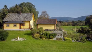 A yellow house with a grey roof and a smaller adjacent building with a red roof, surrounded by green fields and trees. - Gulehuset by Interhome (Reksteren)