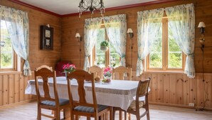 A dining room with a wooden table and chairs, a chandelier, and windows with floral curtains. - Gulehuset by Interhome (Reksteren)