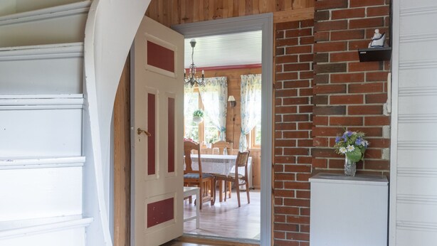 An interior with a wooden ceiling, a brick wall, and a white door leading to a dining area with a table and chairs. - Gulehuset by Interhome (Reksteren)
