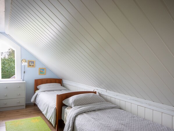 A bedroom with a sloped ceiling, a wooden bed, a dresser, and a window with a view of trees. - Gulehuset by Interhome (Reksteren)