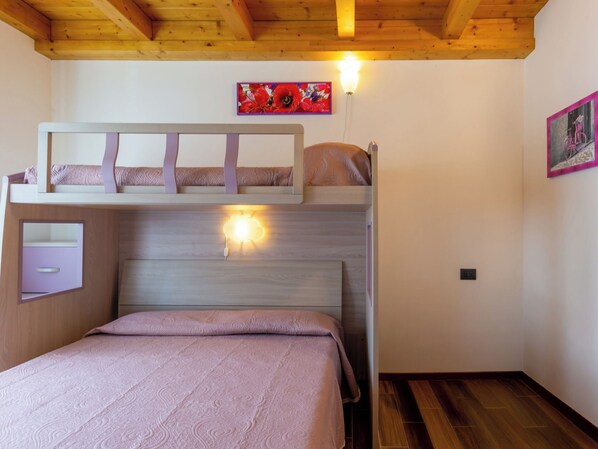 A bunk bed room with a wooden ceiling, a bedside table, and a wall-mounted light. - Gelsomini (CCO522) by Interhome (Colico)