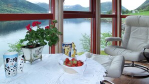 Ein Zimmer mit Seeblick, ein Tisch mit Erdbeeren in einer Schale, ein Stuhl und ein Blumentopf.