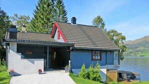 Eine Blockhütte am Seeufer mit einem Schotterweg, einem Steg, der ins Wasser führt, und einem Schild mit der Aufschrift 'Strand'.