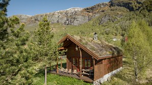 A wooden cabin with a sloped roof, a deck with chairs, and a view of a mountainous landscape.