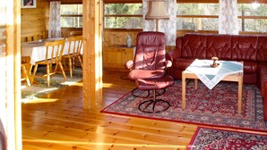 A wooden cabin interior with a dining table, chairs, a red leather sofa, a small table with a lamp, and a patterned rug. - Sandvikfjellet by Interhome (Eikefjord)