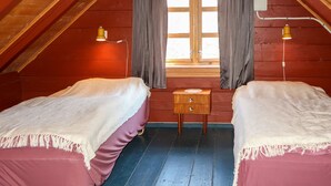 Un dormitorio ático pequeño y acogedor con dos camas individuales, un aparador de madera y una ventana con cortinas.