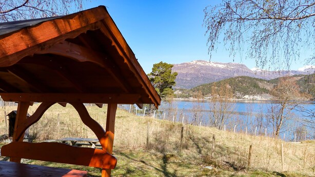 Una mesa de picnic de madera y un refugio junto a un lago, con montañas al fondo.
