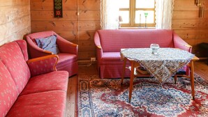 Una habitación acogedora con paredes de madera, un sofá rojo estampado, un sillón a juego, una mesita con superficie de vidrio y una alfombra con diseño.