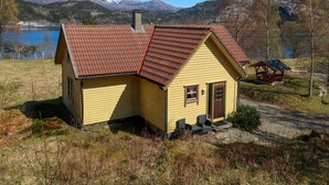 Una casa amarilla con techo marrón, una chimenea y un porche pequeño con dos sillas.