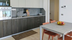 A modern kitchen with dark wood cabinets, a built-in oven, and a dining area with a table and chairs. - Orchidea (GLA126) by Interhome (Gera Lario)