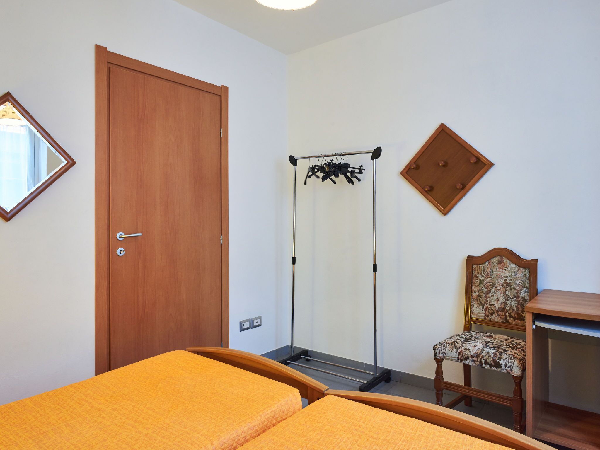 Ein Schlafzimmer mit zwei Betten, einer Holztür, einem Spiegel, einem Stuhl und einem Kleiderschrank.