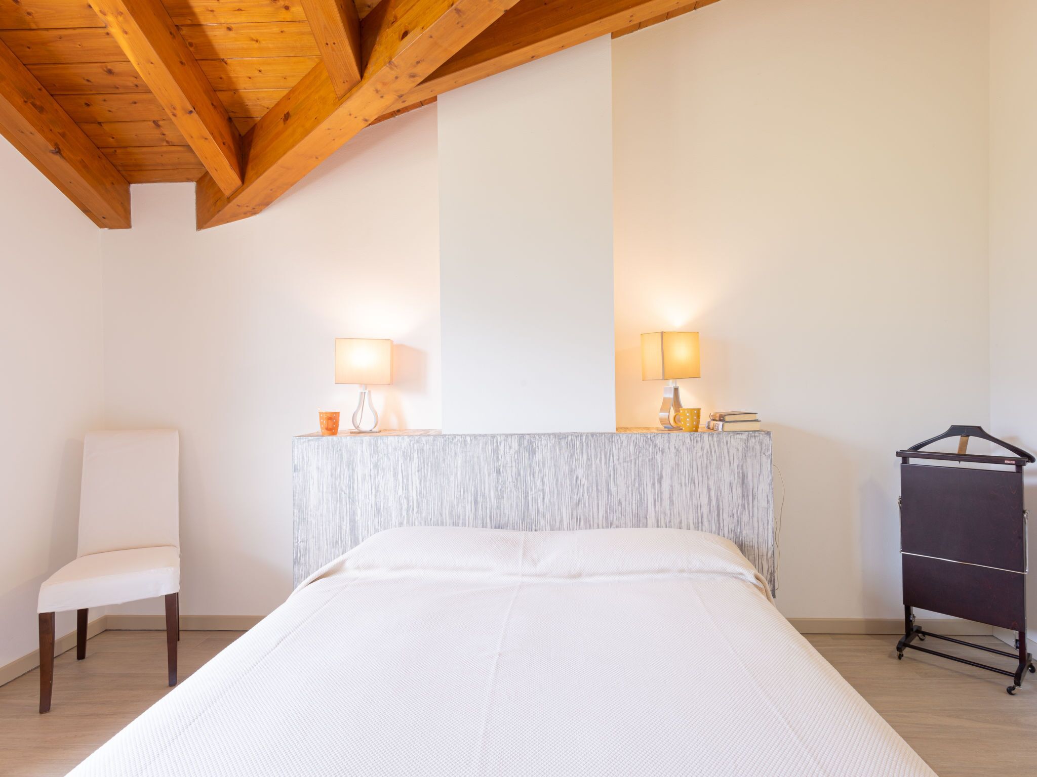 A bedroom with a bed, a chair, a bedside table with lamps, and a coat rack.