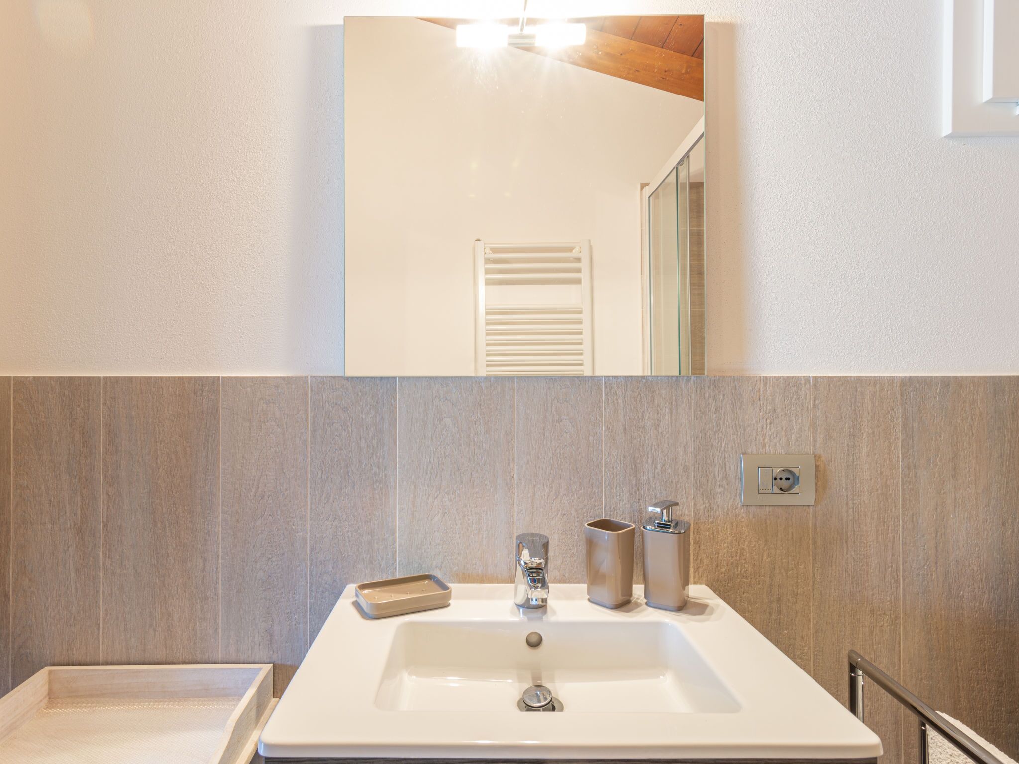 A bathroom with a white sink, a mirror above it, and a wooden wall.
