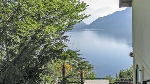 Une vue sur un lac, avec des montagnes en arrière-plan, un arbre au premier plan et un bâtiment doté d’un balcon.