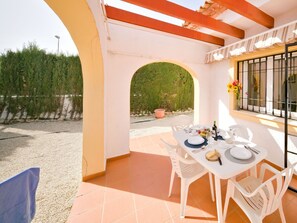 Une terrasse ensoleillée avec une table dressée pour le repas, entourée de chaises blanches, et offrant une vue sur un paysage verdoyant luxuriant.